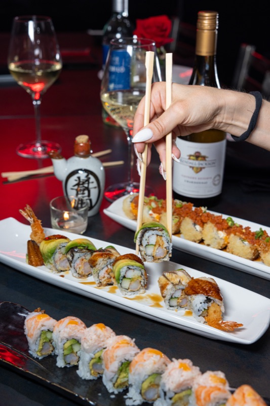 Sushi rolls and wine, chopsticks lifting a piece