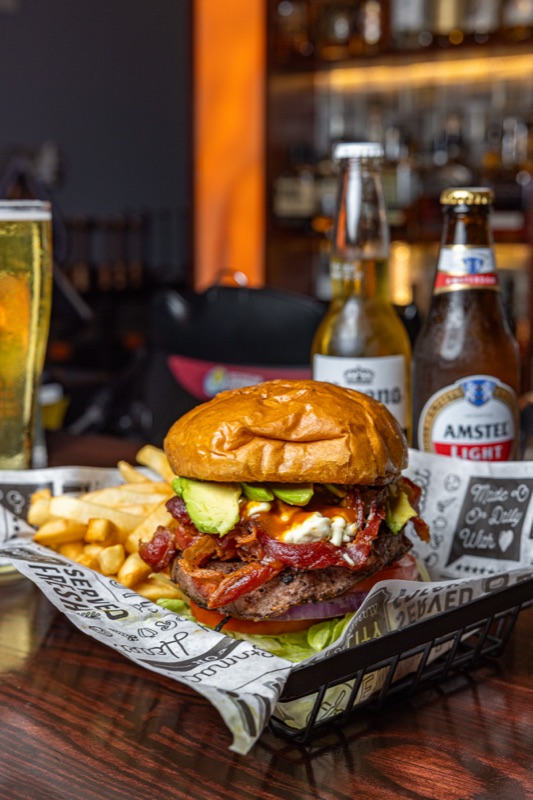 A bacon avocado burger with fries and beer at a bar