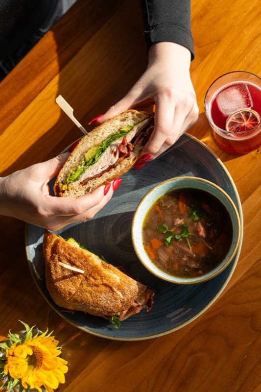 Hands holding a sandwich over a bowl of soup
